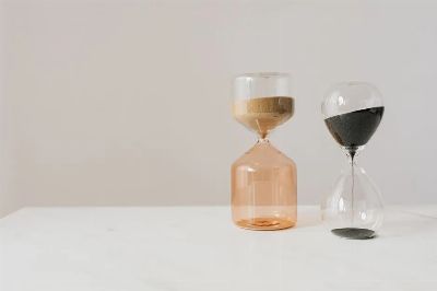 Decorative hourglasses in different shapes with pouring beige and black sand placed on white table