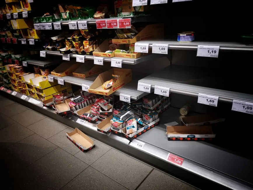 Supermarket shelves largely bare, with printed price labels still in place along the shelf edges