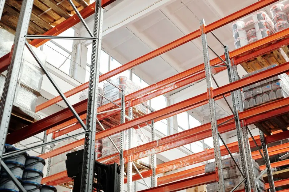 Tall orange warehouse racking holding palletised goods seen from below, illustrating a report on a maximum-severity flaw in an enterprise commerce platform.