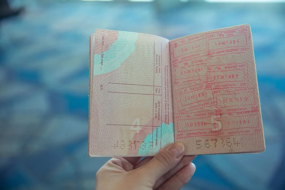 An open passport held up to the light, its visa pages covered in overlapping inked entry and exit stamps.