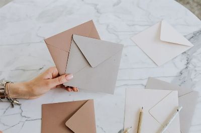 A hand holding craft envelopes on a stylish marble table with pencils, showcasing an artistic layout.