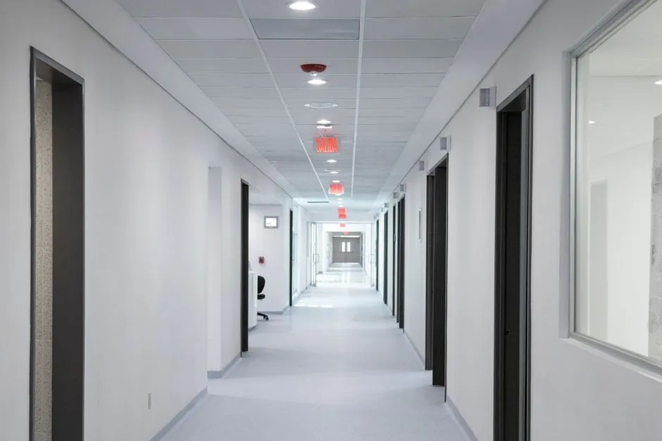 An empty clinical corridor lined with closed doors under fluorescent light, illustrating a report on medical offices shut by a ransomware attack.