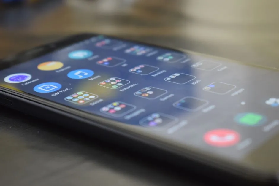 An Android phone lying at an angle showing a home screen of app folders, illustrating a report on developer verification reaching four launch markets.