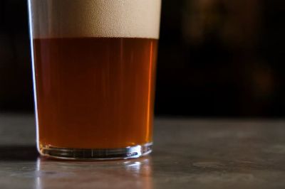 A detailed shot of a glass of amber craft beer topped with foam, set against a dark background.