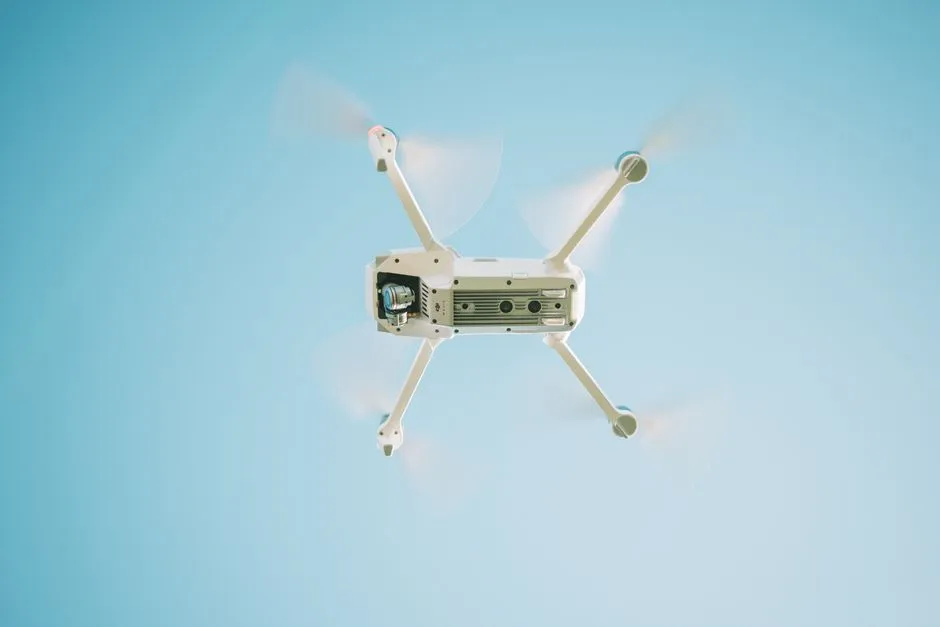 A white quadcopter drone hovering against a pale blue sky, illustrating a report on the expansion of a parcel drone delivery network.