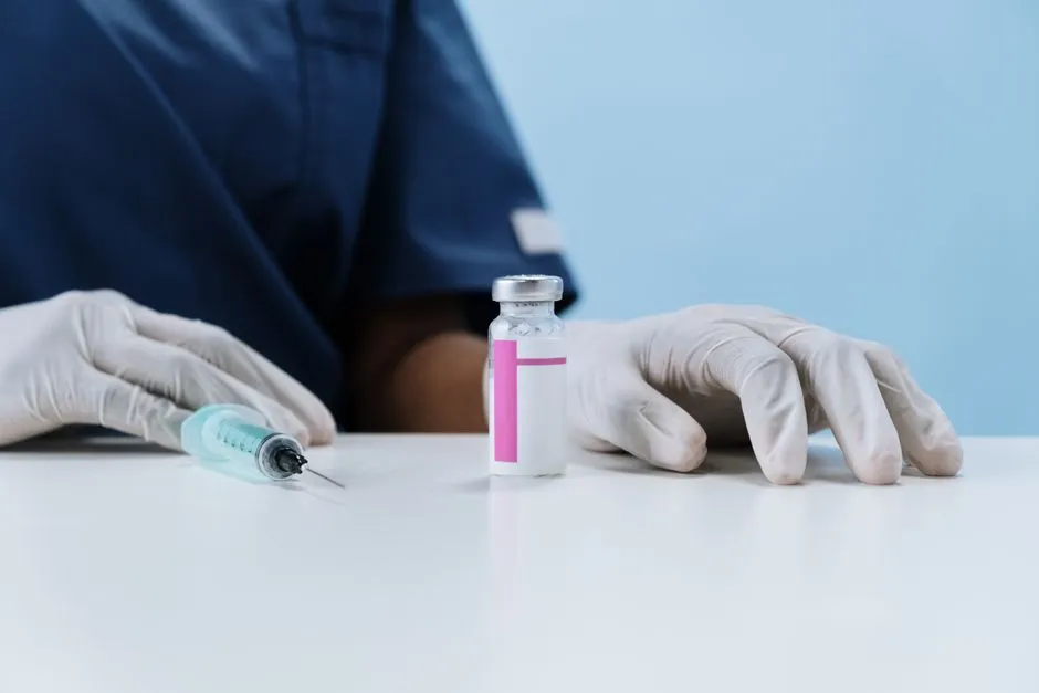 Gloved hands beside a syringe and a labelled vaccine vial on a clinic table