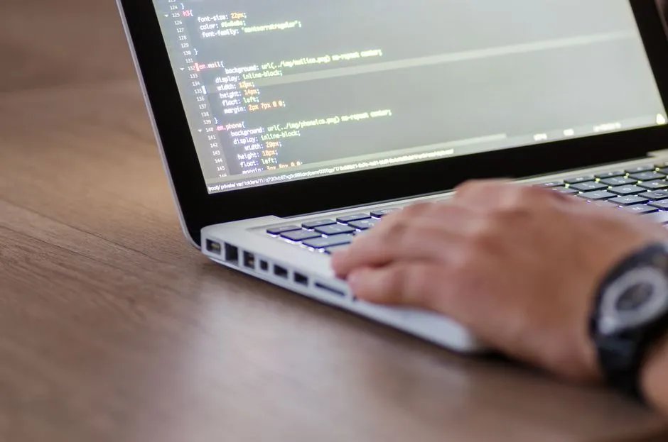 Hands typing on a laptop showing lines of code