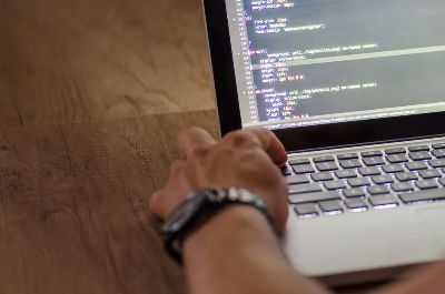 A developer's hand interacting with code on a laptop screen in a workspace setting.
