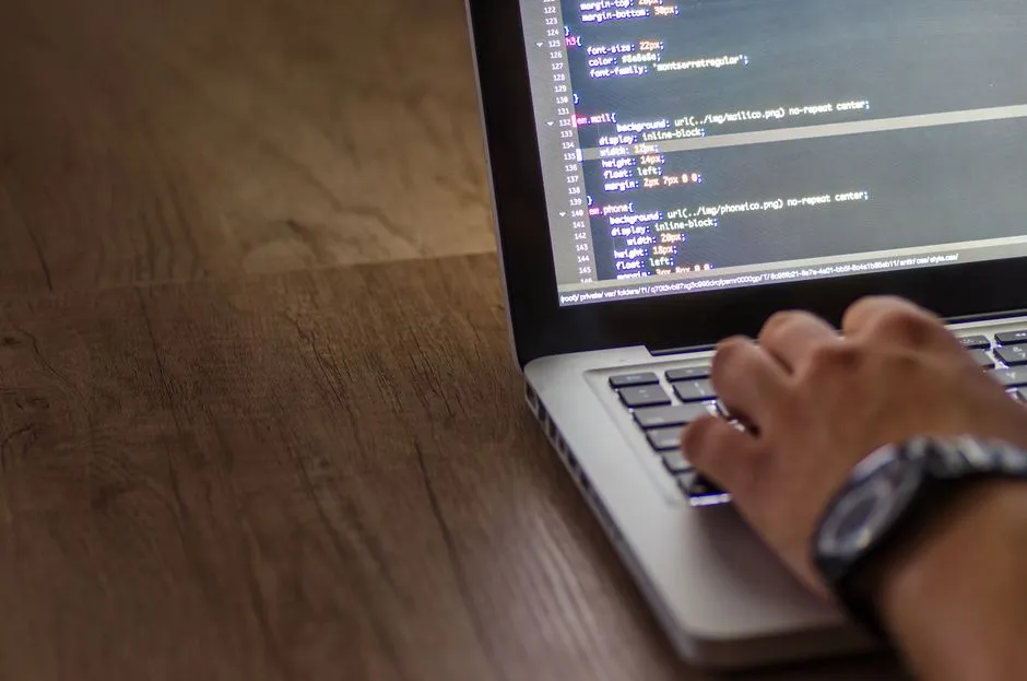 A person is typing code on a laptop, focusing on the screen with programming script.