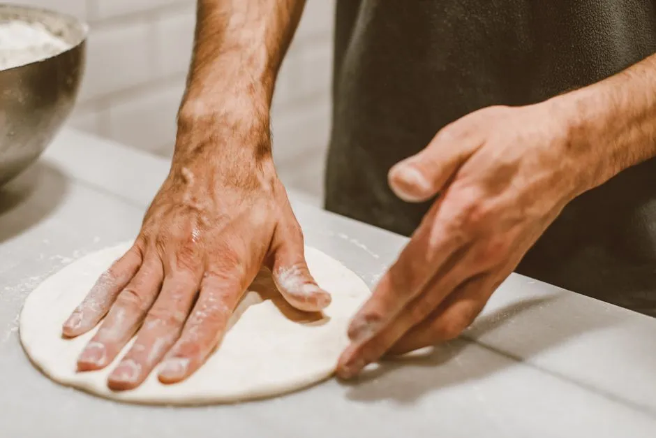 Two hands pressing out a round of pizza dough on a floured counter