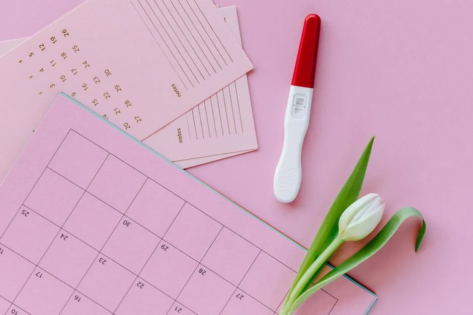A pregnancy test and a white tulip resting on a pink calendar page