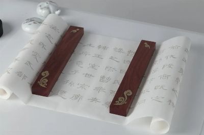 Elegant Chinese calligraphy script on a rolled paper with ornate wooden holders, showcasing traditional art.