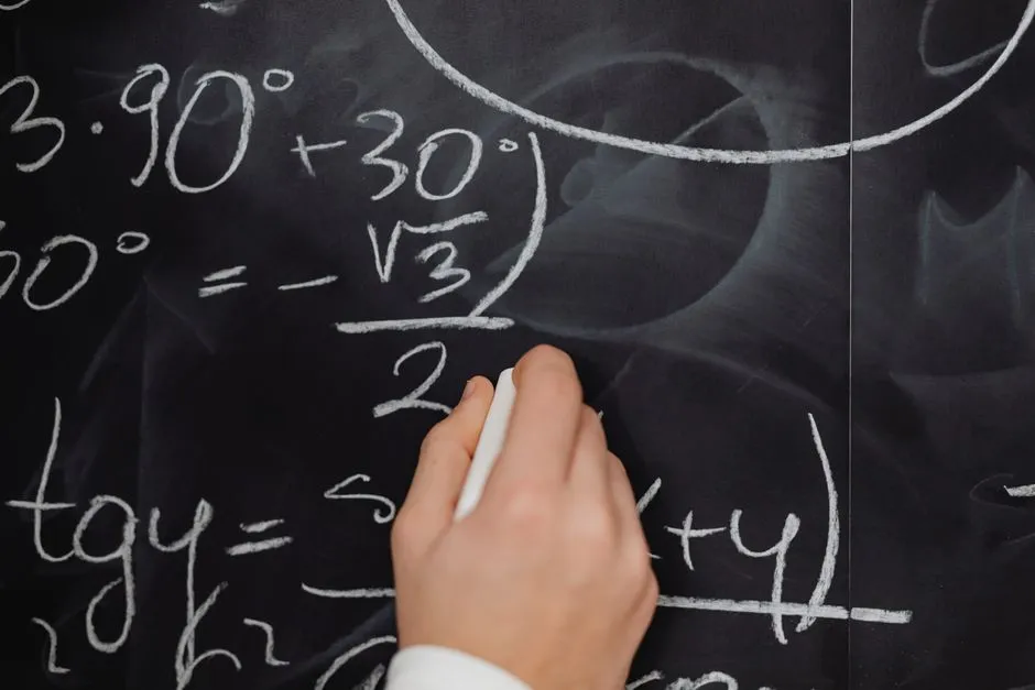 A hand writing trigonometric expressions in chalk on a dark blackboard.