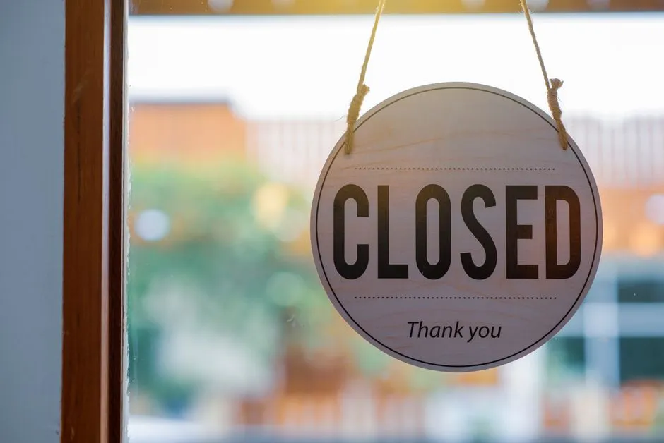 Wooden closed sign hanging on a shop window, with blurred background outside.