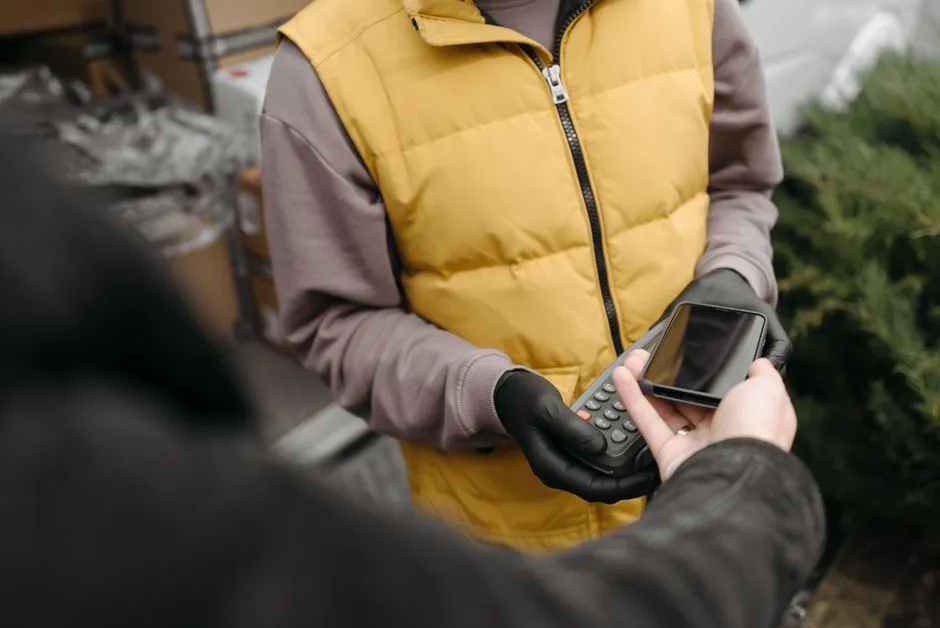 Outdoor delivery person processing contactless payment with a smartphone and terminal.