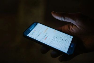 Close-up of a hand holding a smartphone with a messaging app open, illuminated by screen light.