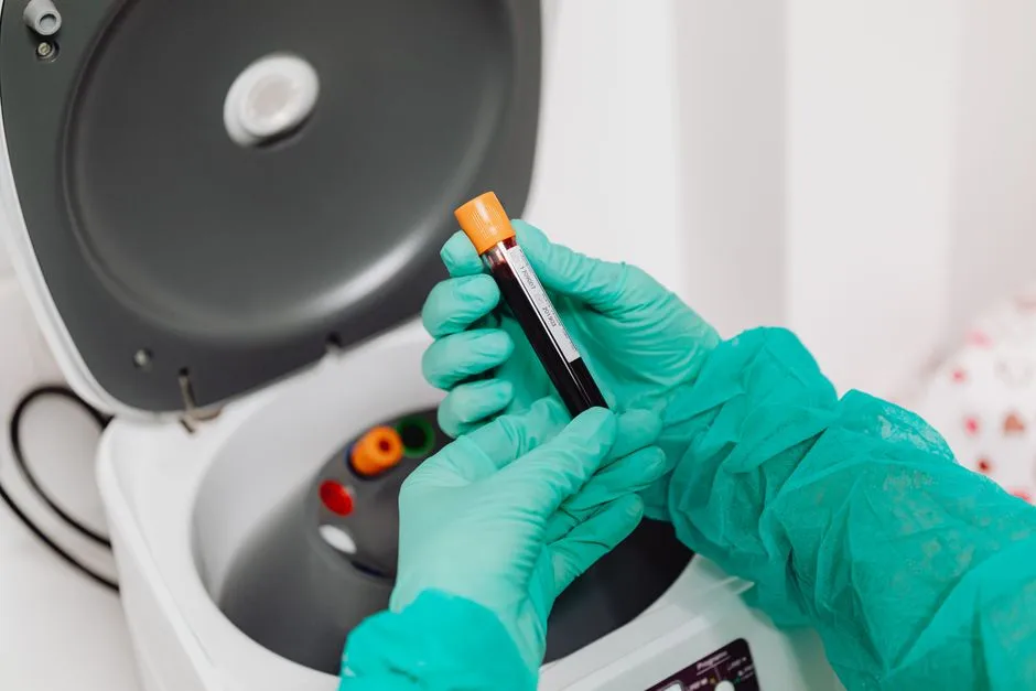 A gloved laboratory worker loading a blood sample tube into a benchtop centrifuge