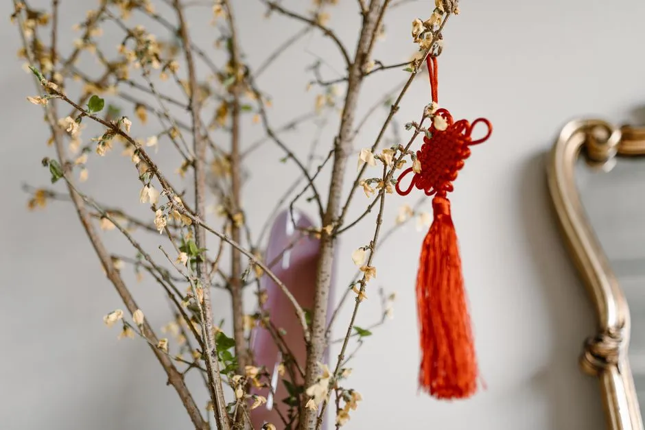 A red Chinese knot with a long tassel hanging from a flowering branch