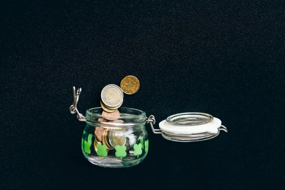Coins dropping into a small glass jar against a black background