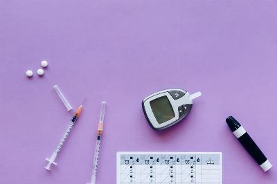 Flat lay of diabetes management tools including glucometer, syringes, and pills on purple background.