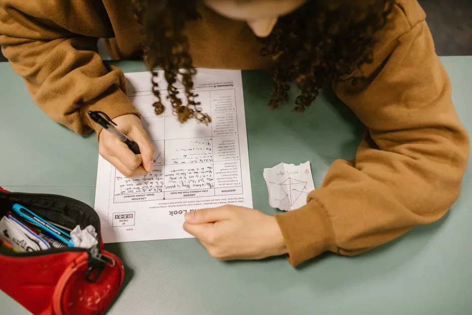 Overhead view of a student writing on an exam paper at a desk.