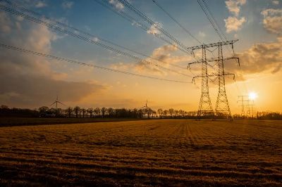 Captivating sunset scene featuring windmills and power lines over a vast agricultural field.