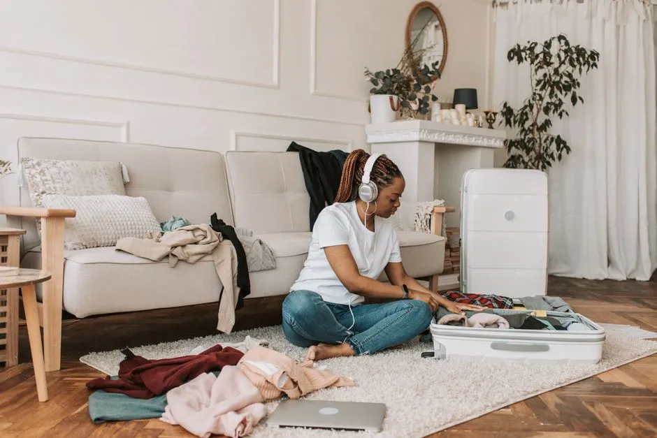 A woman sitting on a living-room floor packing clothes into an open suitcase