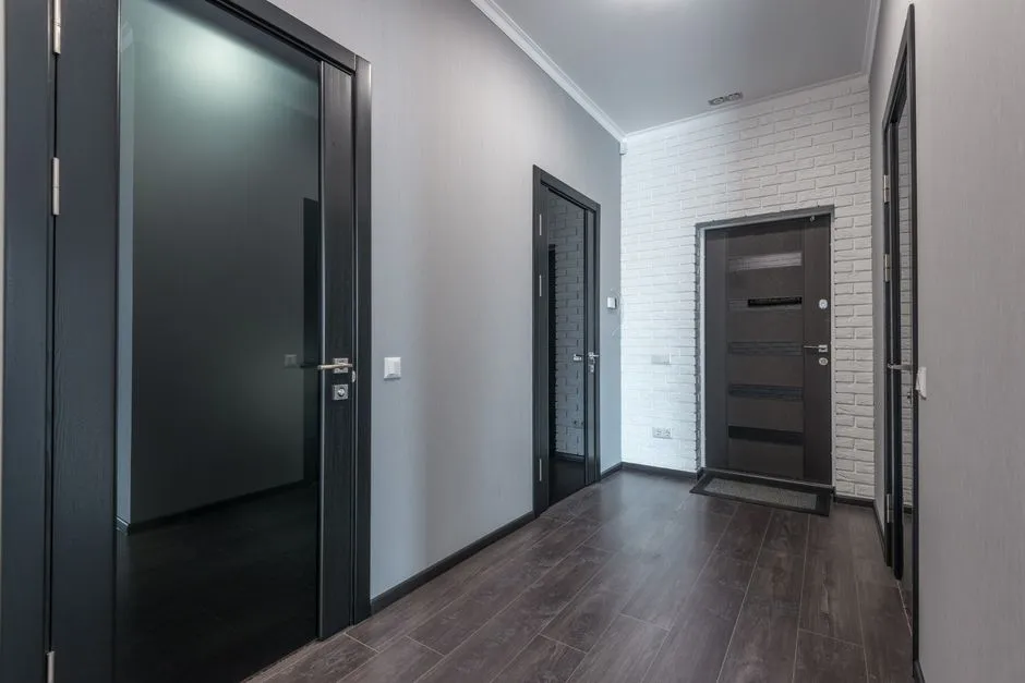 A corridor lined with several identical dark doors, one standing open