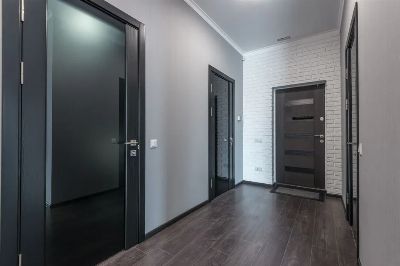 Interior of empty spacious corridor with laminate floor and black doors with glass parts and white ceiling and gray painted…