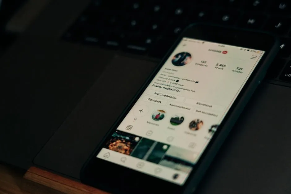 A phone resting on a laptop keyboard, showing a social-media profile page with follower counts and a grid of posts
