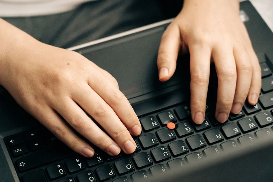 Two hands typing on a black laptop keyboard, photographed from above.