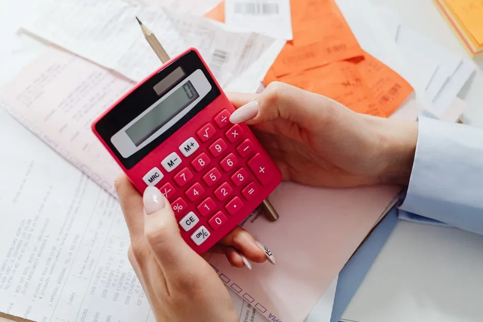 A person working through printed paperwork with a red desk calculator.