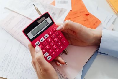 Close-up of hands holding a red calculator, managing finances with documents and receipts.