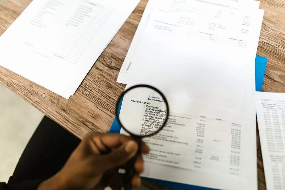 A hand holding a magnifying glass over printed records on a desk — illustrating the self-audit this report describes.