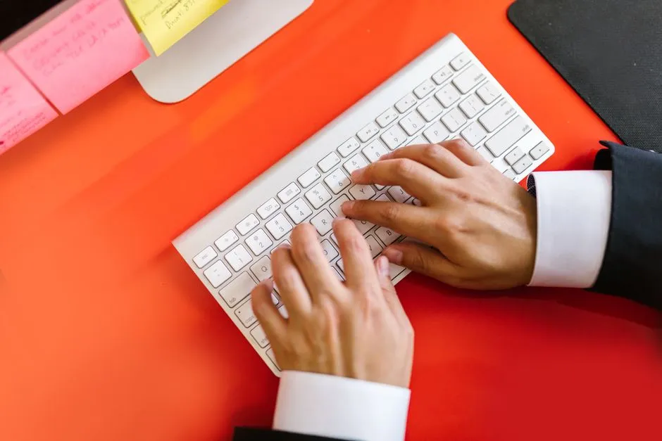 Two hands typing on a white keyboard on an orange desk