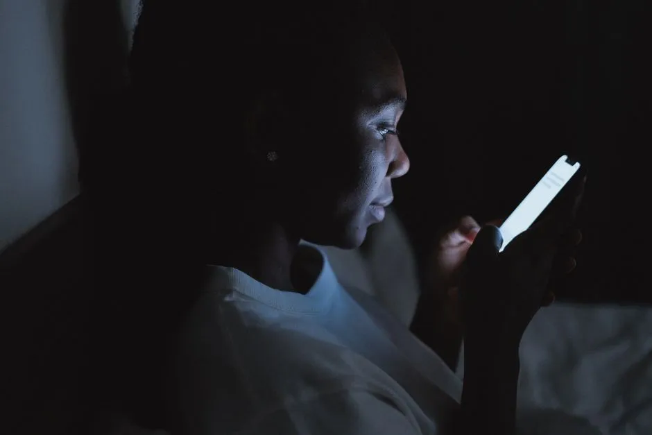 A person lying in a darkened room, their face lit only by the screen of the phone they are holding.