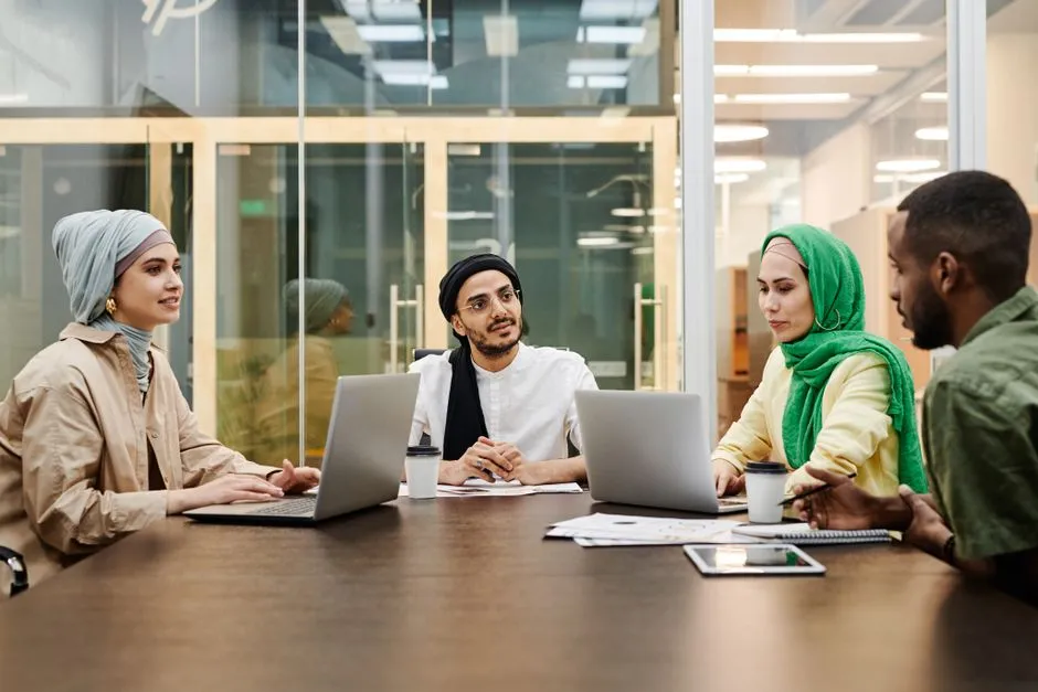 Four colleagues talking across a boardroom table with laptops, illustrating a report on IBM's new OpenAI consulting practice.
