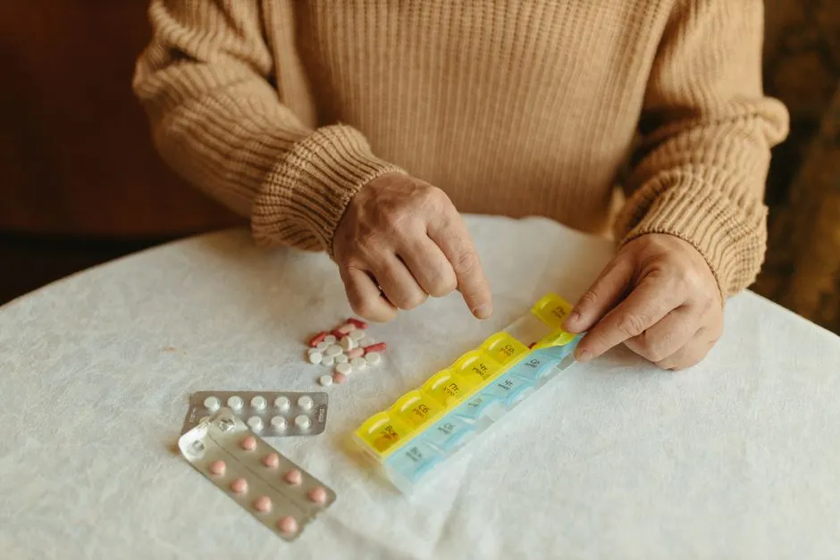 An older person's hands sorting tablets from blister packs into the compartments of a yellow weekly pill organiser on a table.