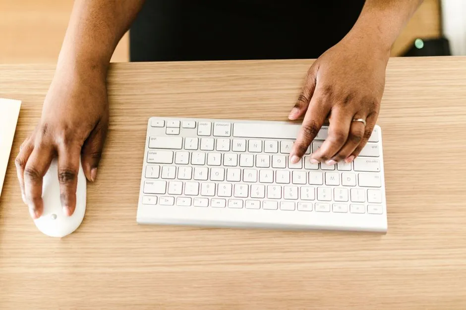 A pair of hands at a keyboard and mouse on a wooden desk, seen from above