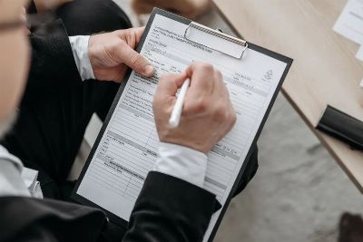 Close-up of a businessman signing a formal document on a clipboard.