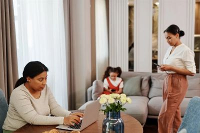 A woman works on a laptop while others use devices in a cozy living room setting.