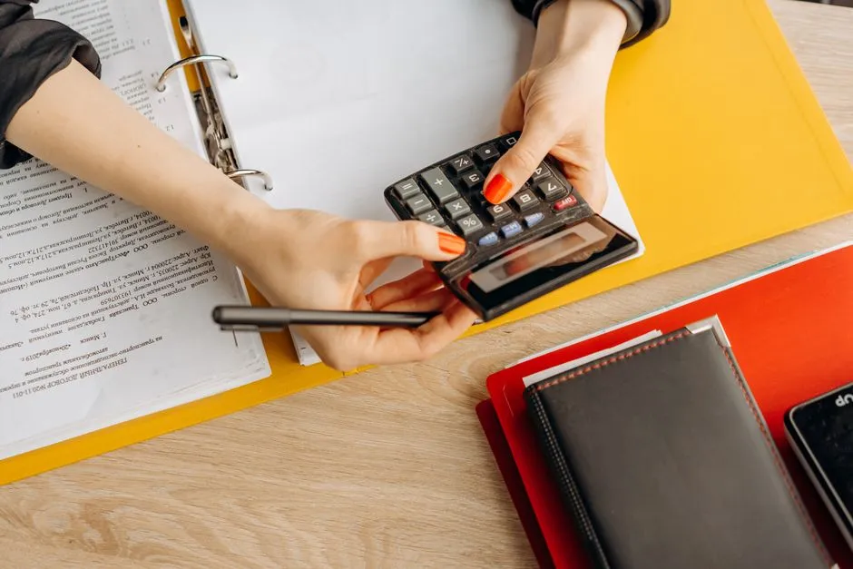 Hands using a calculator beside documents and folders, illustrating a report on a fund buying accounting firms to run AI through them.