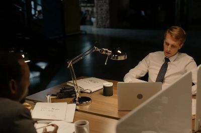 Two professionals working late in an office, reviewing documents under a desk lamp.