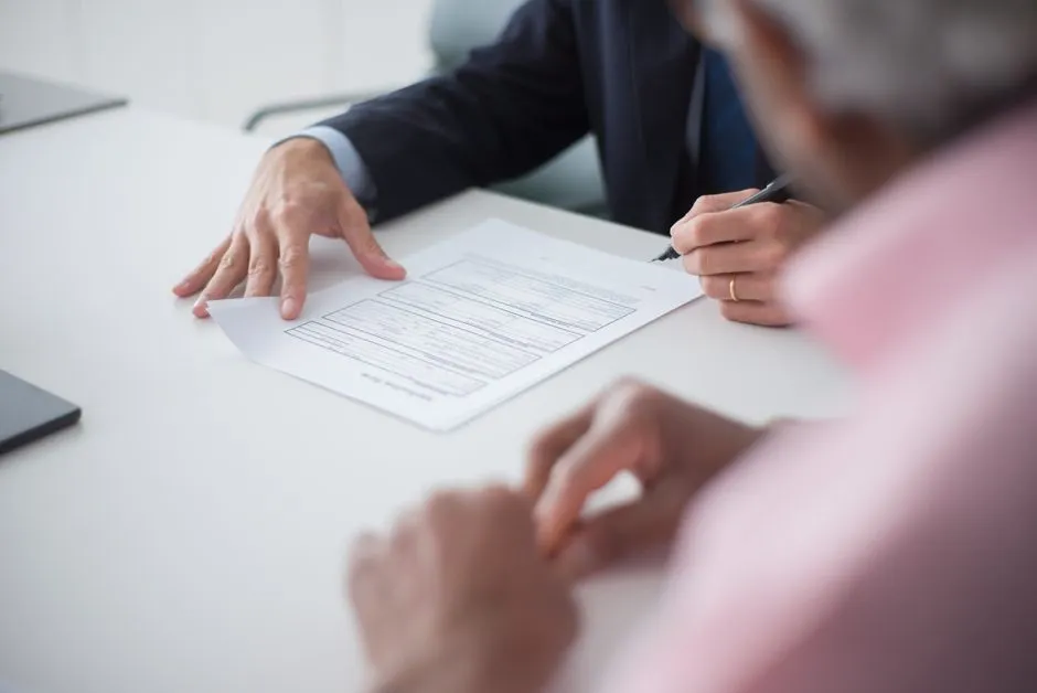 Hands over a document being signed across a desk, illustrating a report on a compute-collateralised financing structure backed by Broadcom guarantees.