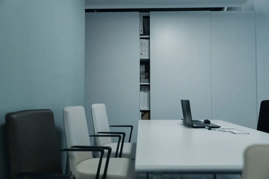 An empty conference room with chairs around a white table, illustrating a report on senior executive departures from OpenAI.