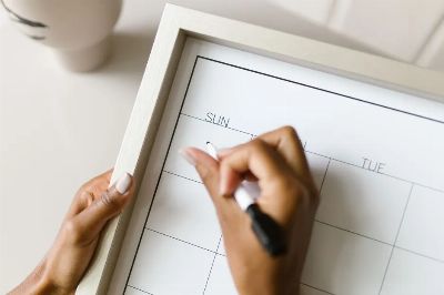 Hands holding a wall calendar, writing with a marker, organizing schedule.