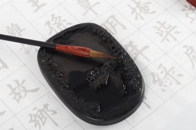Close-up of a Chinese calligraphy brush and ink stone on paper with hieroglyphs.