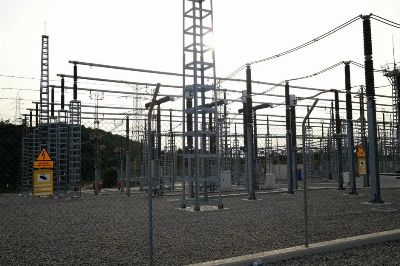 Outdoor electrical power substation with high voltage equipment and safety signs, surrounded by fencing.