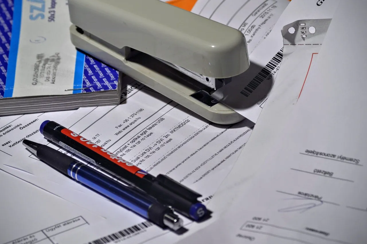 A stapler and pen resting on a stack of printed invoices and forms