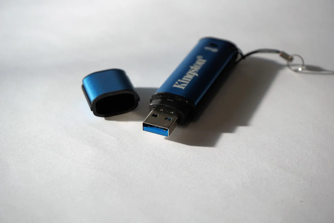 A dark blue USB memory stick lying on a pale surface with its cap removed beside it.